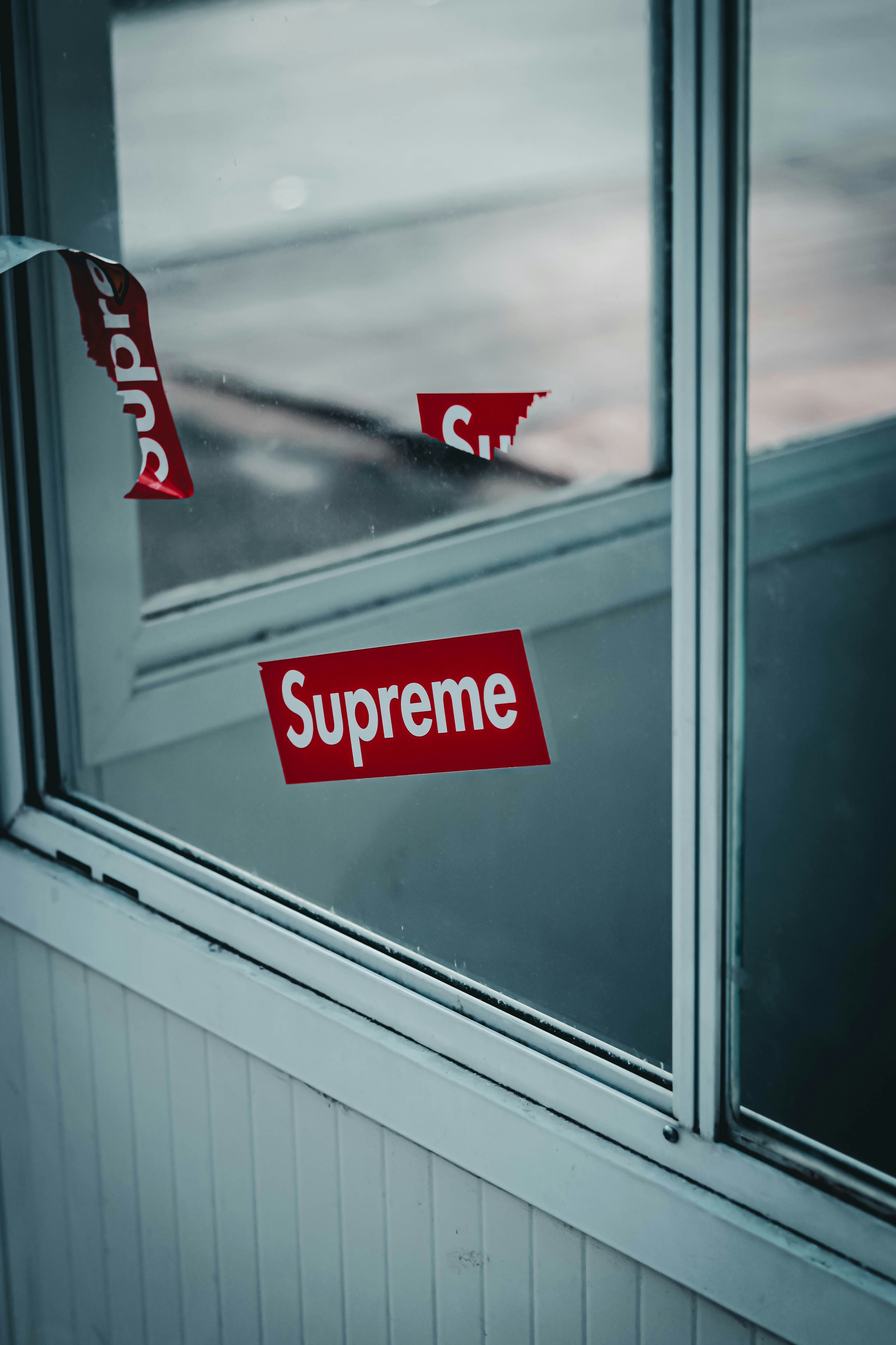 a red supreme sticker sitting on the side of a window