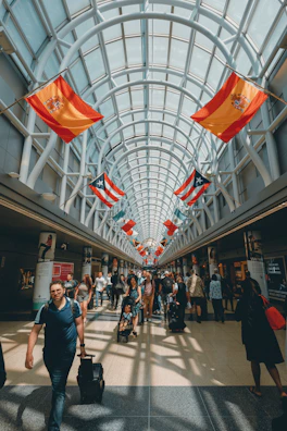 An airport scene with travelers and international flags waving in the breeze.