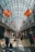 A spacious, well-lit airport corridor lined with various international flags hanging from the ceiling. People of diverse backgrounds are walking, carrying luggage, and pushing strollers. The area is bustling with travelers and the glass ceiling allows natural light to flood the space.