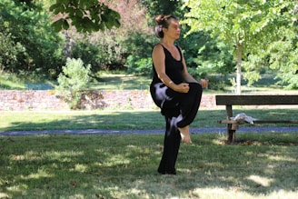 woman in black tank top and black pants sitting on brown wooden bench under green tree
