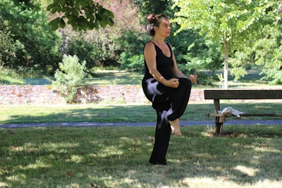 woman in black tank top and black pants sitting on brown wooden bench under green tree