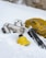 A collection of outdoor equipment is scattered on the snow, including a yellow backpack, a silver thermos, a kettle, and poles with black handles. Snow covers the ground, creating a cold and serene atmosphere.