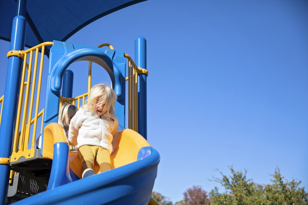 menina na camisa amarela que monta o slide plástico azul durante o dia