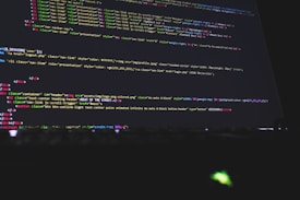 Colorful code is displayed on a computer screen, featuring a mix of HTML and CSS elements with syntax highlighting. The text is organized in lines and the colors indicate different tags and attributes, including classes and style properties.