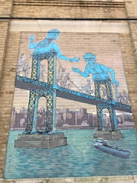 A mural featuring a stylized bridge with two large blue figures integrated into the bridge's structure, reaching out towards each other. Below them, smaller figures appear to be walking across the bridge while a cityscape background and water body are visible. A ship is seen sailing beneath the bridge.