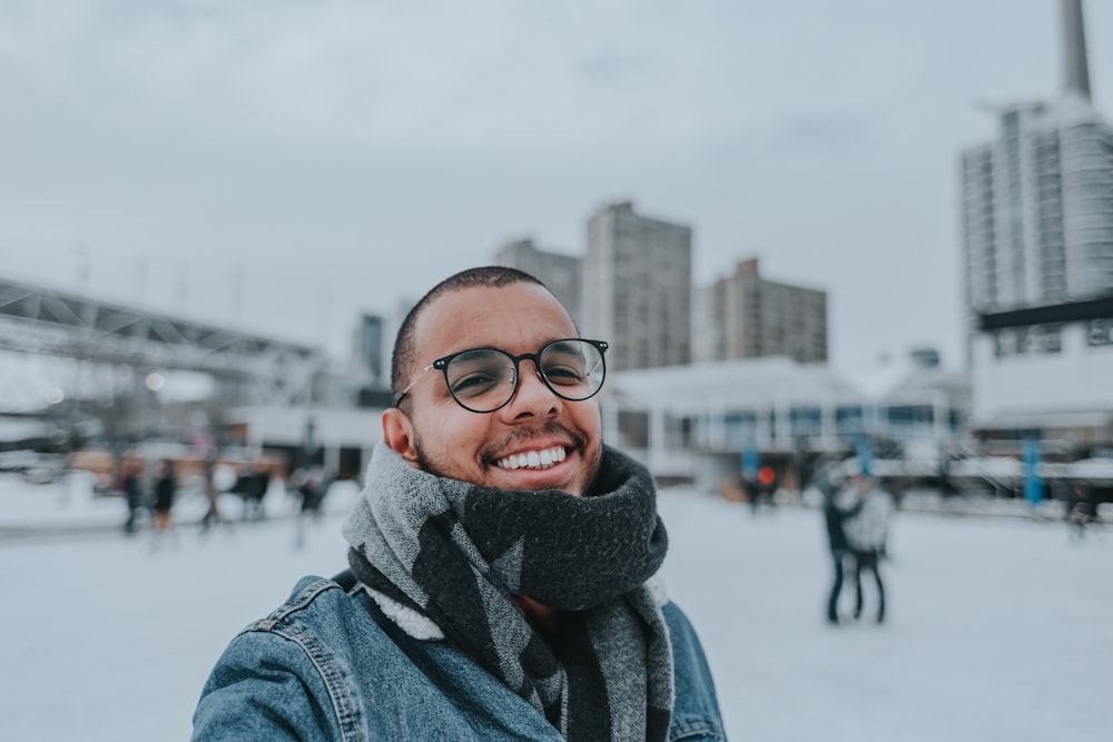 Un homme portant des lunettes et un foulard sourit à la caméra