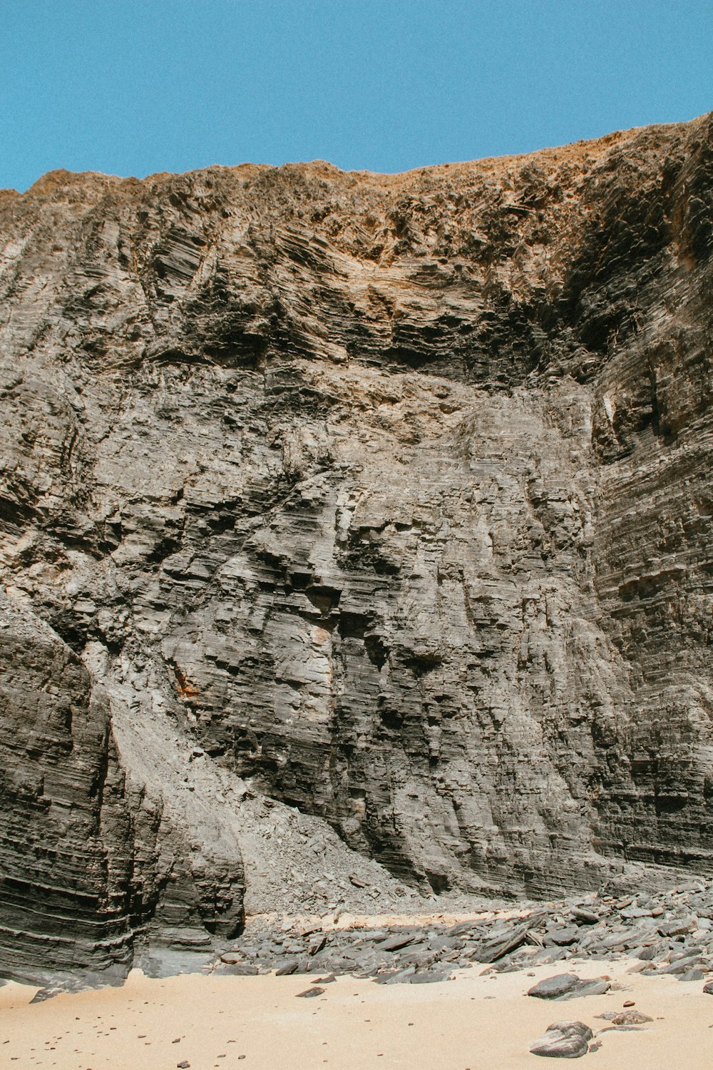 a rocky cliff face on a beach with footprints in the sand