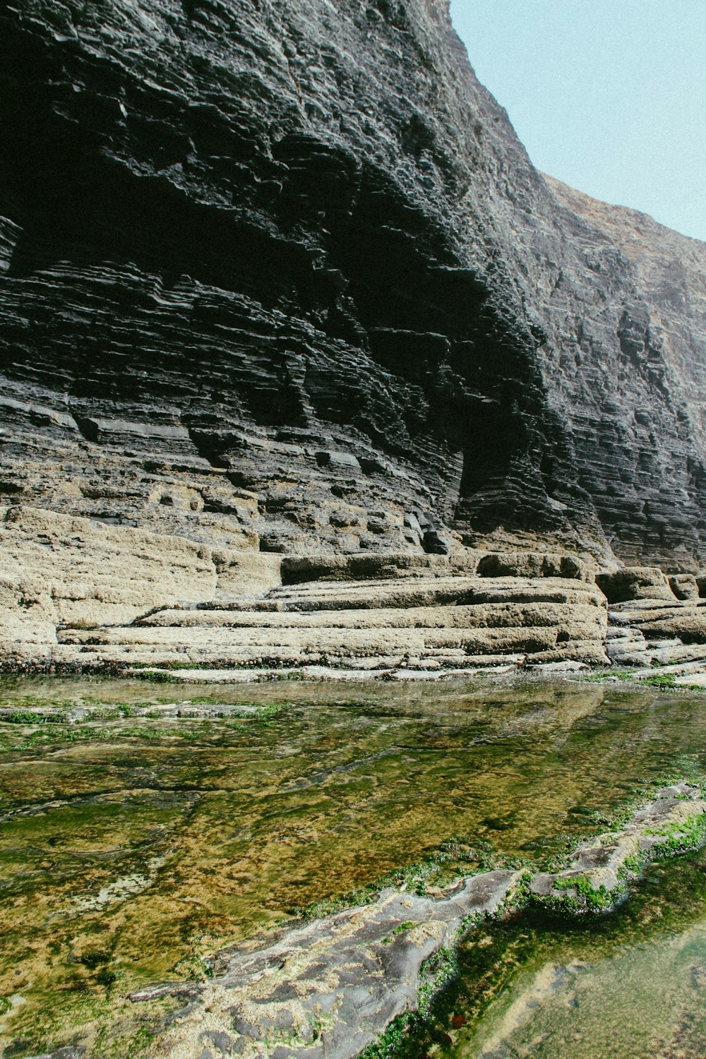 a rocky cliff with a body of water in front of it