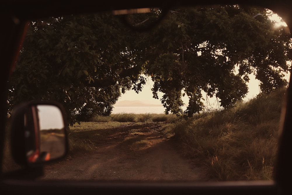 a view of a dirt road through a rear view mirror