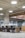 An open office space with several black swivel chairs placed around a long wooden table with light grey carpet on the floor. The ceiling design features exposed pipes and round white ceiling lights which create a modern, industrial look. Large glass walls line one side of the room.