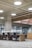 An open office space with several black swivel chairs placed around a long wooden table with light grey carpet on the floor. The ceiling design features exposed pipes and round white ceiling lights which create a modern, industrial look. Large glass walls line one side of the room.