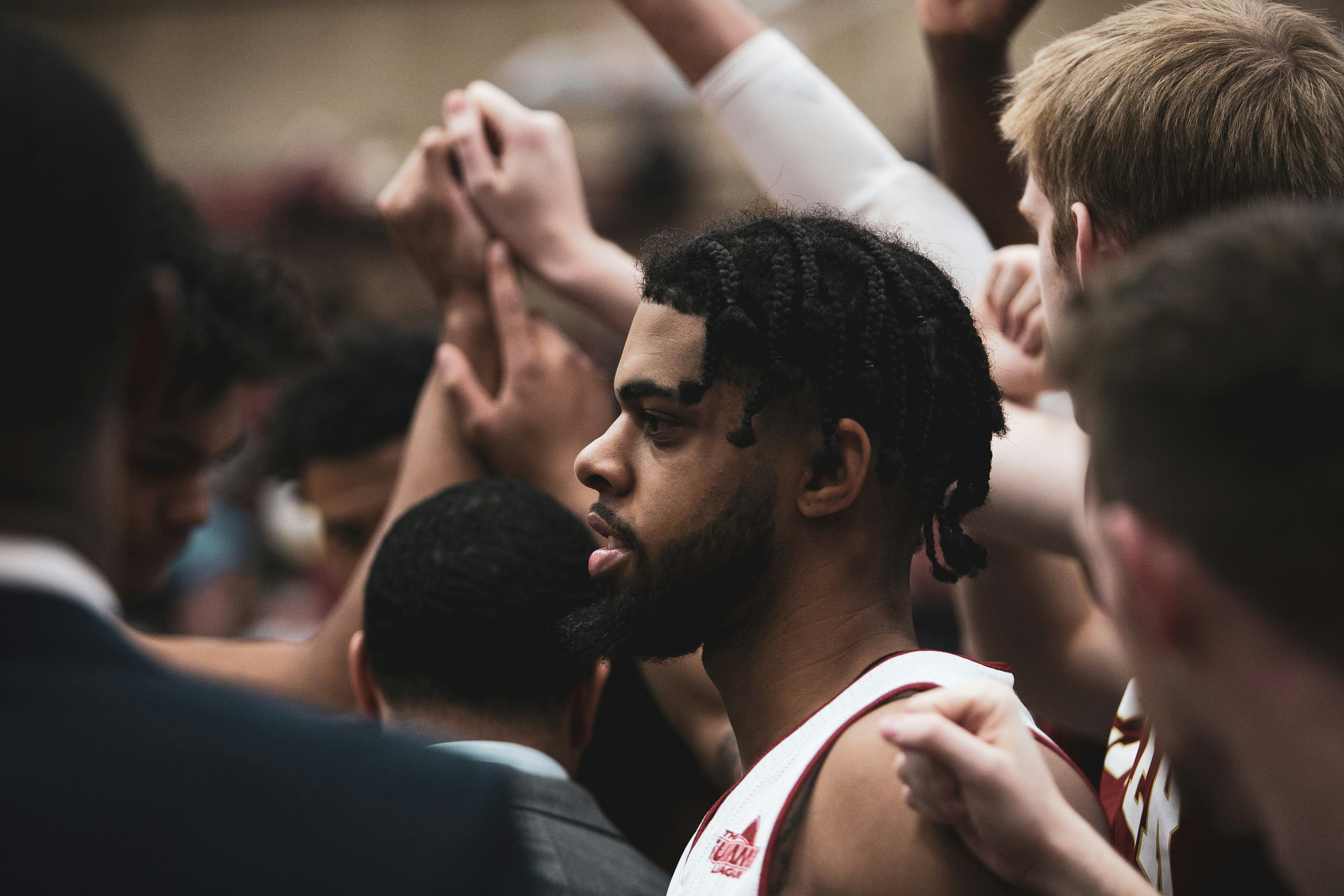 Basketball players and coaches in a huddle, hands raised in unity.