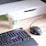 A workspace setup with a black RGB gaming keyboard, a black wired gaming mouse, and a white coffee cup with a green logo. The desk has a light wood finish and a white desk organizer is seen in the background.