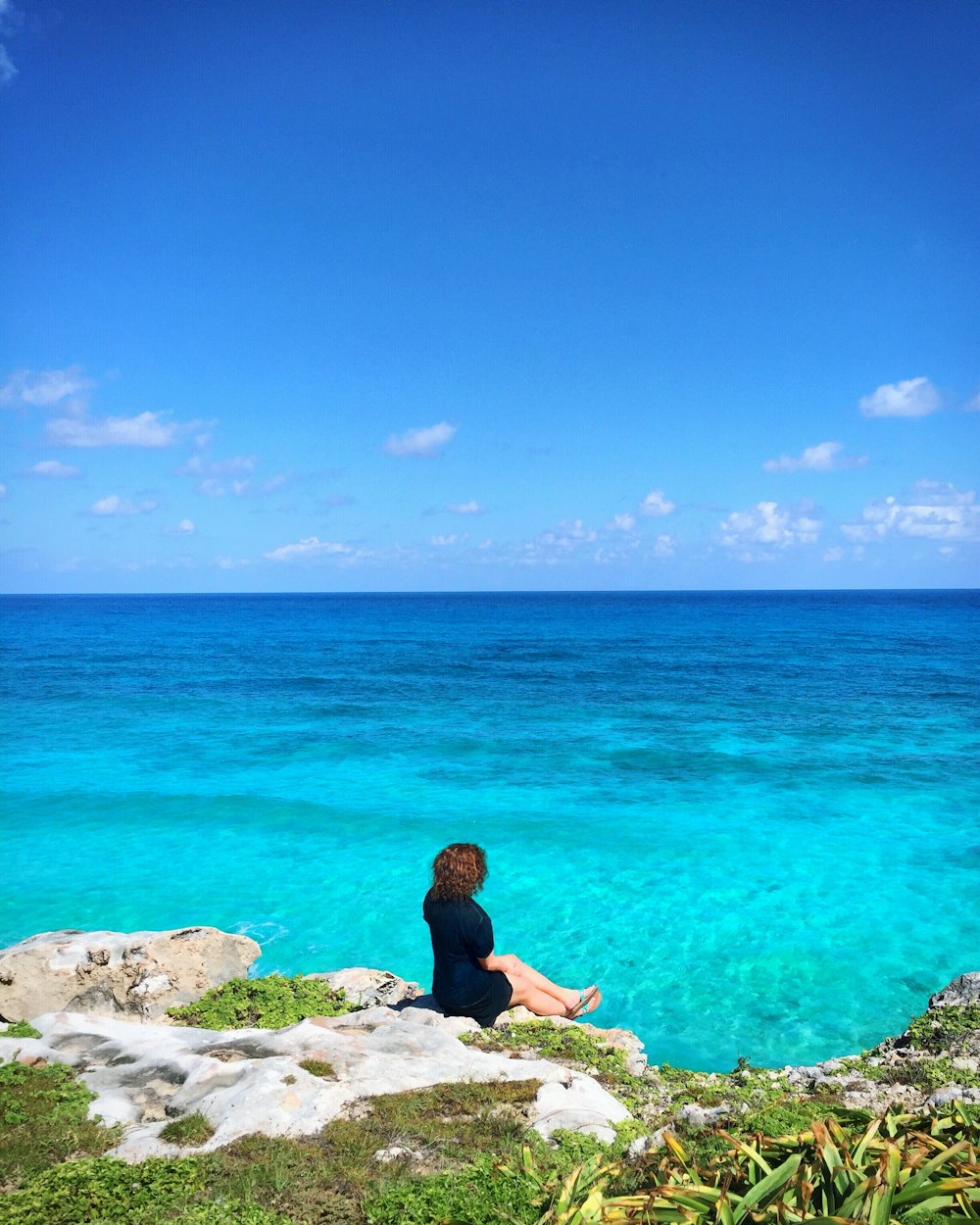 a person sitting on a rock near the ocean