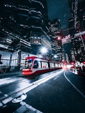 a red and white train traveling through a city at night