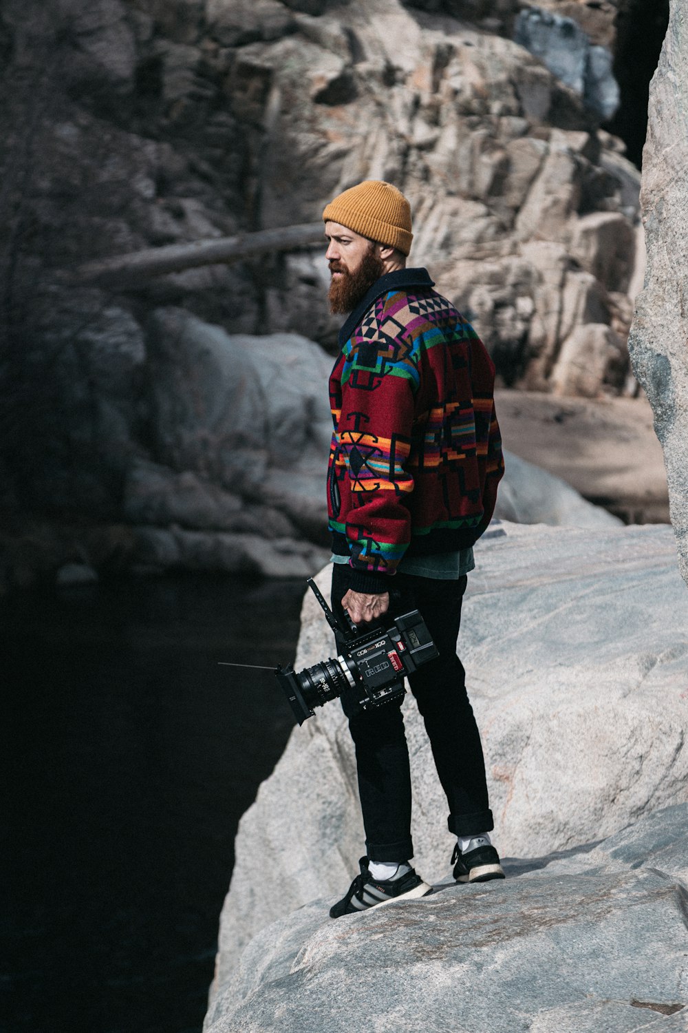 Hombre con camisa de vestir a cuadros rojos y negros y pantalones negros sosteniendo una cámara DSLR negra