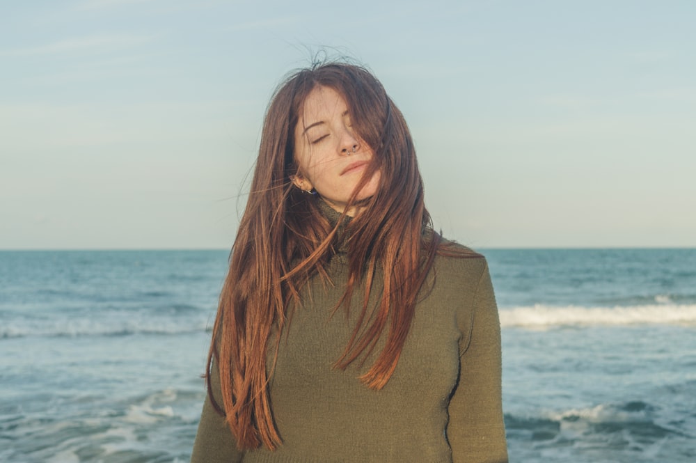 woman in brown turtleneck sweater standing near sea during daytime
