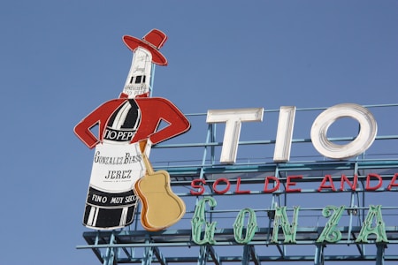 A rooftop billboard against a clear blue sky features a stylized bottle dressed in a red jacket and hat, holding a guitar. The bottle advertises 'Gonzalez Byass Jerez' with the text 'Tio Pepe' on the label. Large letters spell out 'TIO SOL DE ANDA'.