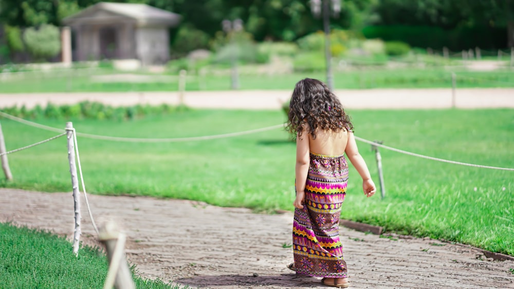 girl in purple and pink dress walking on pathway during daytime