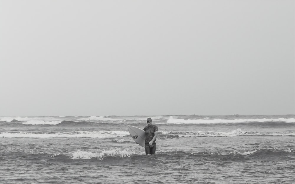 Foto in scala di grigi dell'uomo che tiene la tavola da surf sulla spiaggia