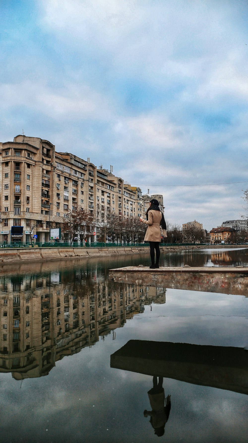 woman in black jacket standing on water near brown concrete building during daytime