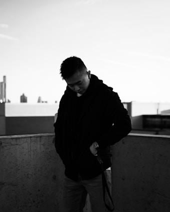 A sleek, modern jacket with refined tailoring hanging on an urban rooftop rail, city skyline in the background at dusk.