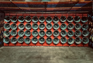 Rows of loudspeakers are mounted on a red wall, each displaying various words, likely indicating language or sound-related themes. The setup exudes a sense of uniformity and organization.