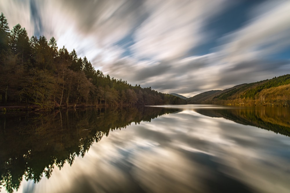 a body of water surrounded by trees under a cloudy sky