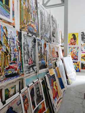 An artist's studio corner with colorful paintings of TV and movie characters leaning against a brick wall.