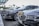 A row of luxury cars parked in an outdoor setting, each adorned with floral arrangements on their fronts. The vehicles are lined up under a modern canopy with a background of palm trees, suggesting a formal or celebratory event.