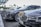 A row of luxury cars parked in an outdoor setting, each adorned with floral arrangements on their fronts. The vehicles are lined up under a modern canopy with a background of palm trees, suggesting a formal or celebratory event.