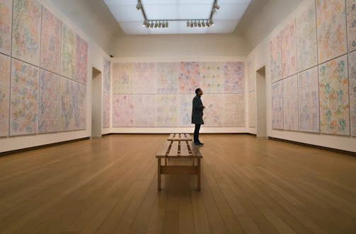 A softly lit corner of the gallery showing a large abstract painting hung above a minimalist wooden bench.