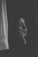 A black-and-white candid shot of a person staring out a window, lost in thought.