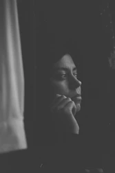 Minimalistic black and white photo of a person reflecting thoughtfully near a window.