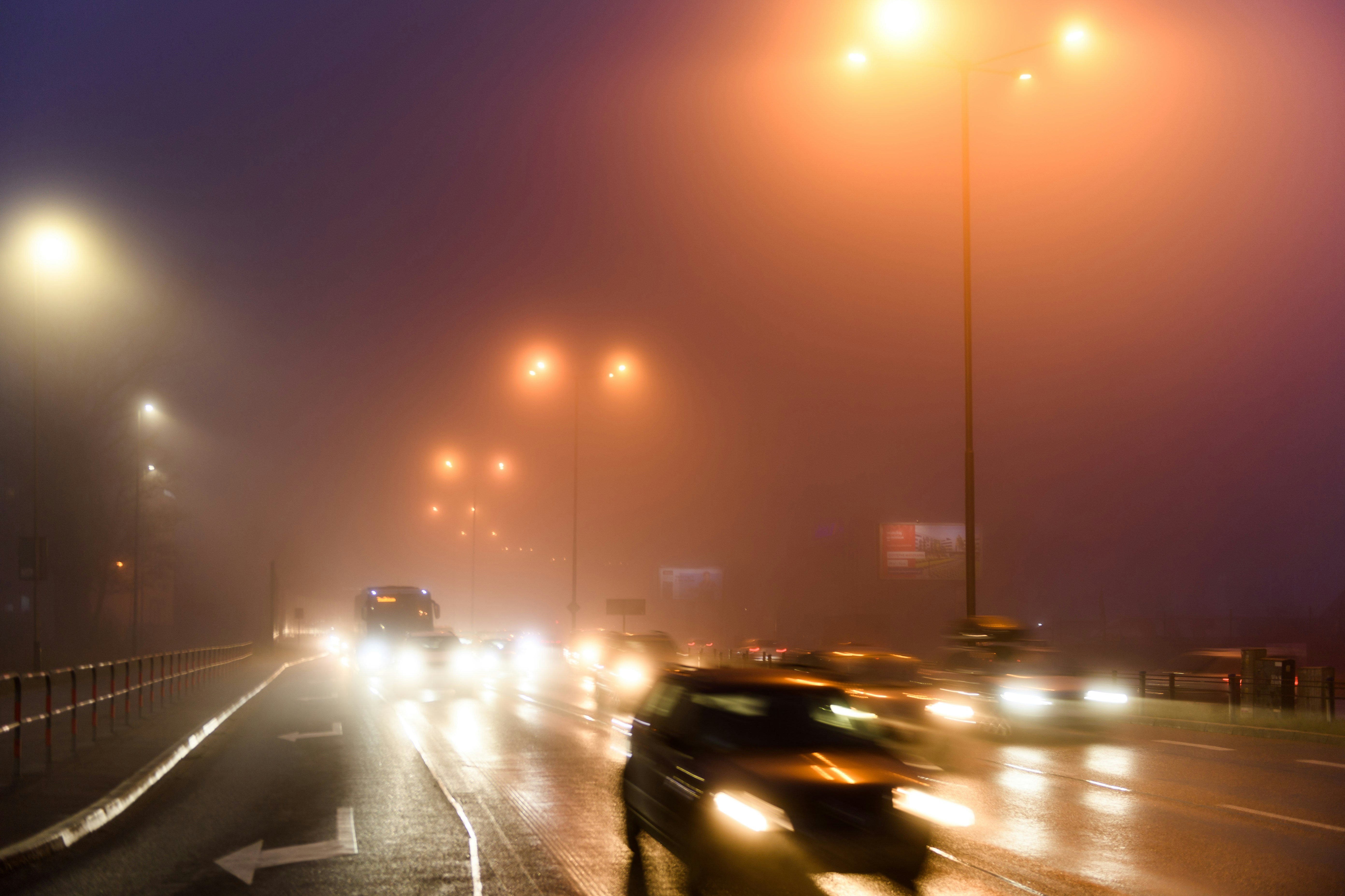 a foggy night with cars driving down the road, Smog and traffic.