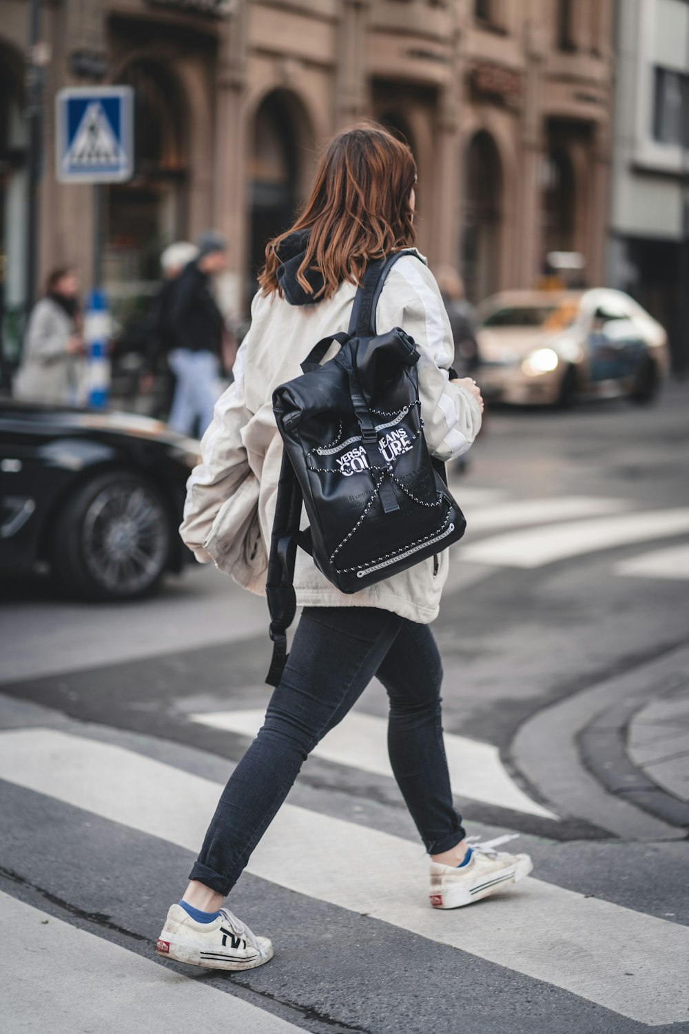 mulher em calças pretas e jaqueta branca andando na calçada durante o dia