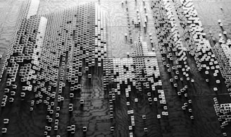 A black and white abstract arrangement of small, three-dimensional square blocks is positioned against a textured background. The blocks vary in height, creating a sense of depth and complexity, with shadows adding to the visual texture. The pattern suggests a digital or futuristic theme, reminiscent of cityscapes or data visualizations.