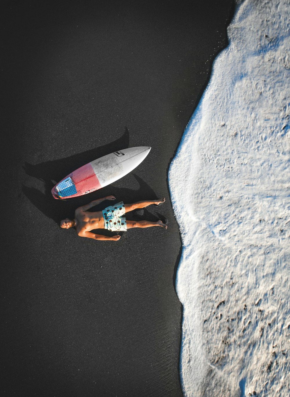 a person laying on a beach next to a surfboard