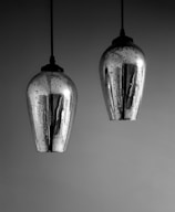 Two metallic pendant lights with a reflective silver surface hang from the ceiling. The lights have a teardrop shape and are speckled with dark spots, creating a textured appearance against a smooth background.