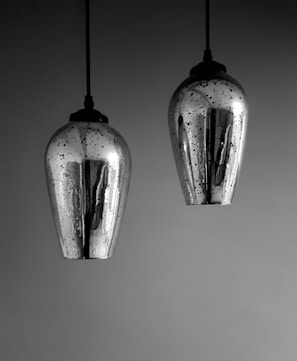 Two metallic pendant lights with a reflective silver surface hang from the ceiling. The lights have a teardrop shape and are speckled with dark spots, creating a textured appearance against a smooth background.