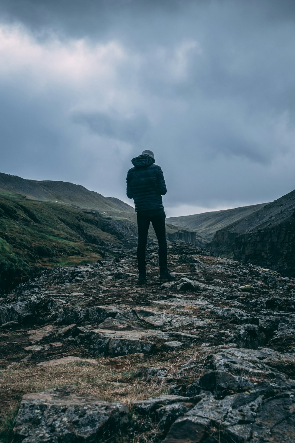 man in black jacket standing on rock formation under gray cloudy sky during daytime