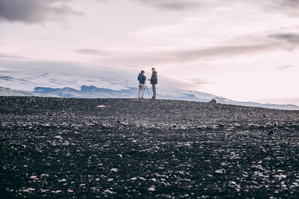 man in black jacket and white pants standing on rocky ground under cloudy sky during daytime