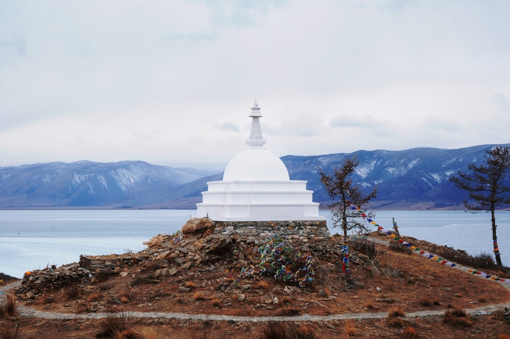 white concrete building on brown field near body of water under white clouds during daytime