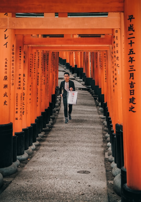 man in white shirt and black pants walking on gray concrete pathway in Fushimi Inari Taisha Japan