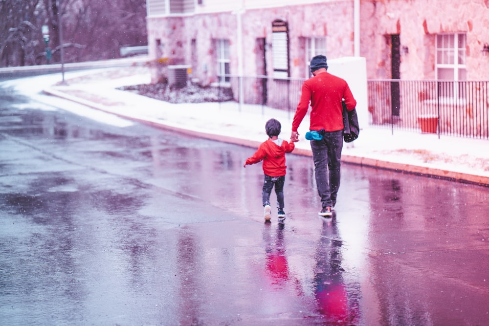 赤いジャケットとブルーデニムジーンズの男性が昼間、濡れた道を歩いている