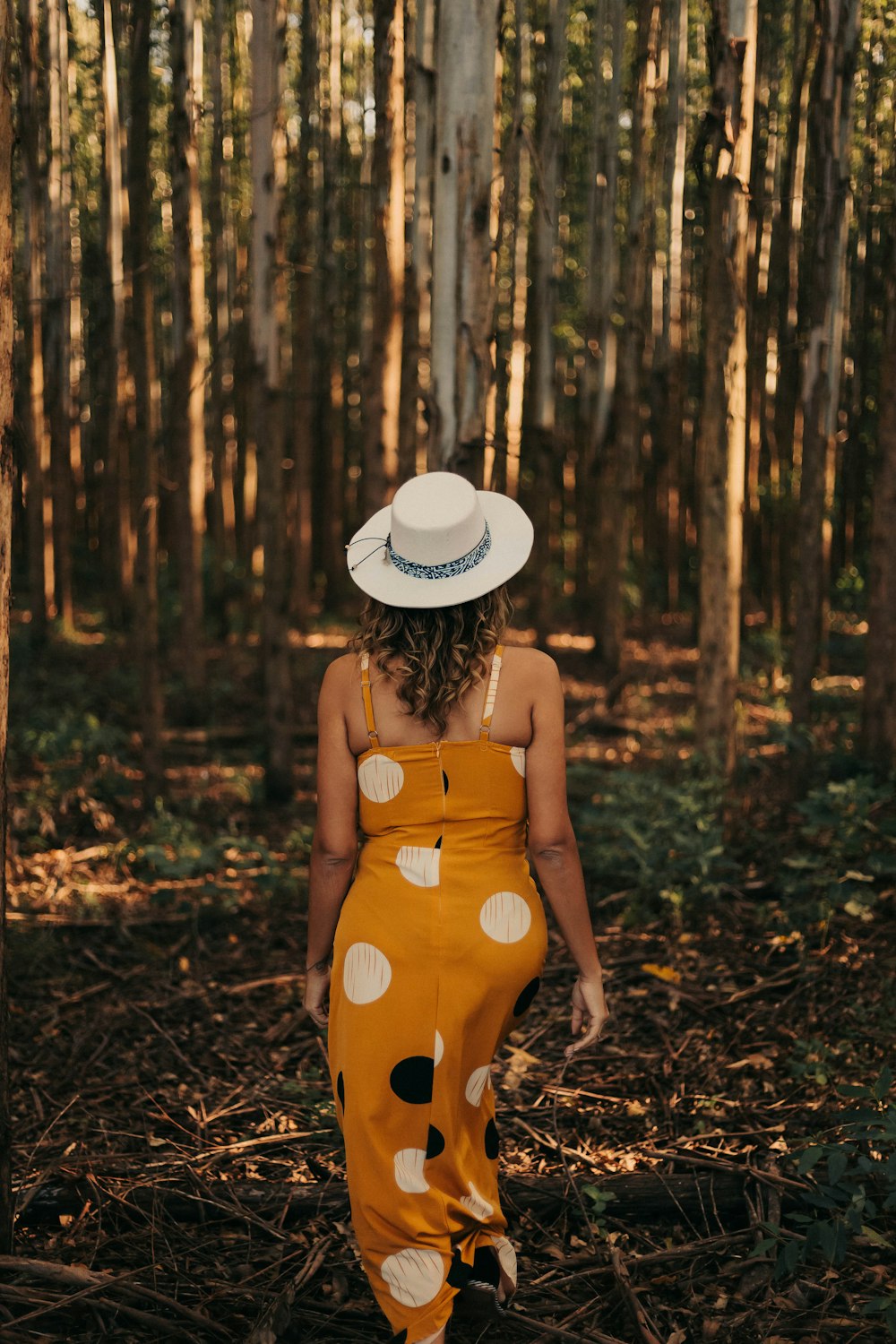 Una donna in un vestito a pois e cappello cammina attraverso i boschi