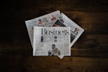 a stack of newspapers sitting on top of a wooden table
