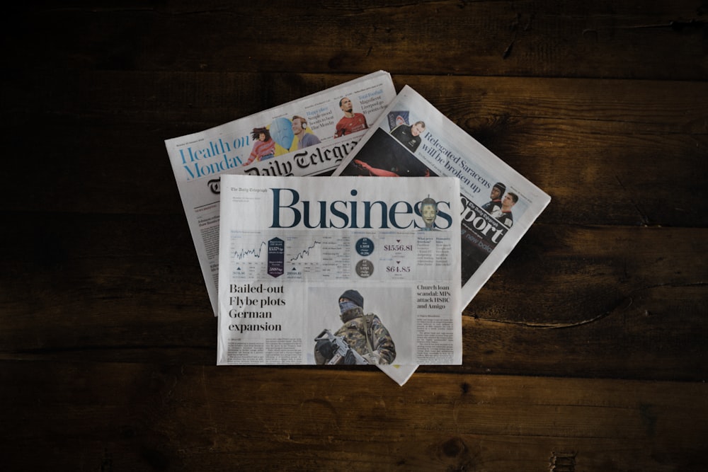 a stack of newspapers sitting on top of a wooden table