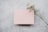 A sprig of delicate white flowers lies diagonally across a soft pink rectangular card placed on a textured gray surface.