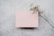 A sprig of delicate white flowers lies diagonally across a soft pink rectangular card placed on a textured gray surface.